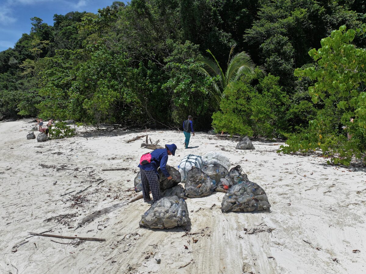 A volunteer ties up full bags of rubbish on the sand at the edge of the jungle.